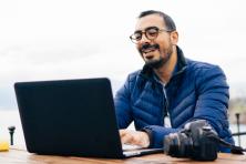 man sitting outside with laptop and camera